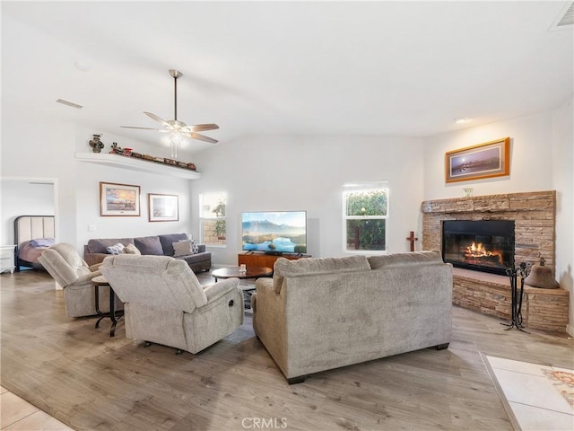 living area featuring visible vents, lofted ceiling, light wood-style floors, and a stone fireplace