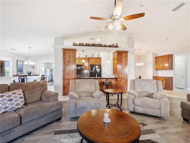 living area featuring visible vents, ceiling fan with notable chandelier, light wood-style flooring, and vaulted ceiling