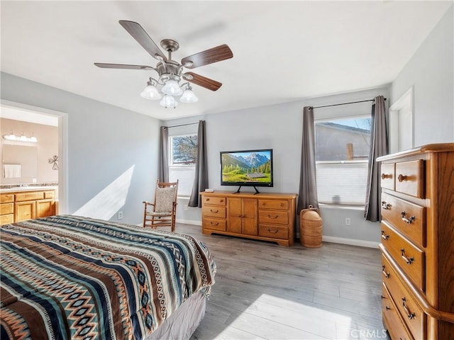 bedroom featuring baseboards, light wood-type flooring, ensuite bathroom, and ceiling fan