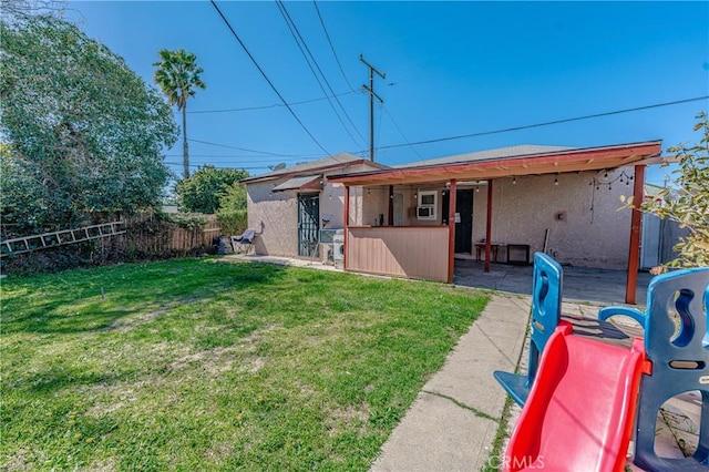 rear view of house featuring a patio area, a yard, fence, and stucco siding