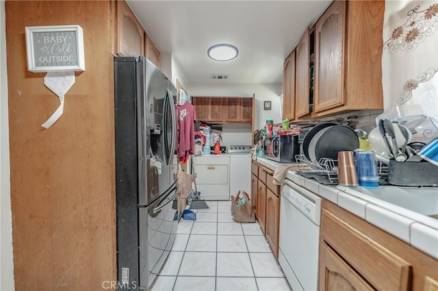 kitchen featuring light tile patterned flooring, separate washer and dryer, tile counters, appliances with stainless steel finishes, and brown cabinets