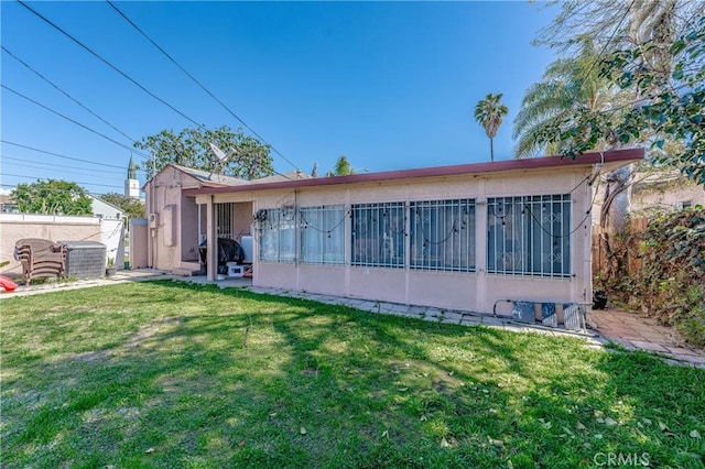 back of house featuring stucco siding, a lawn, and fence