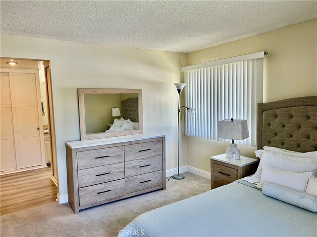 bedroom featuring a textured ceiling, baseboards, and light carpet