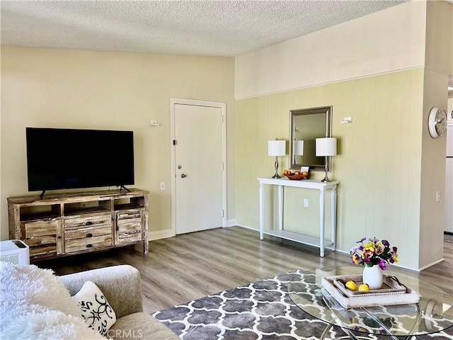 living area featuring vaulted ceiling, a textured ceiling, baseboards, and wood finished floors