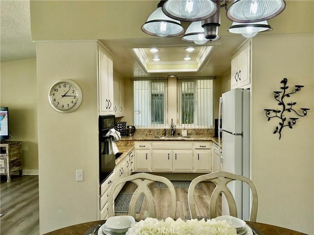 kitchen featuring crown molding, a tray ceiling, freestanding refrigerator, white cabinets, and a sink