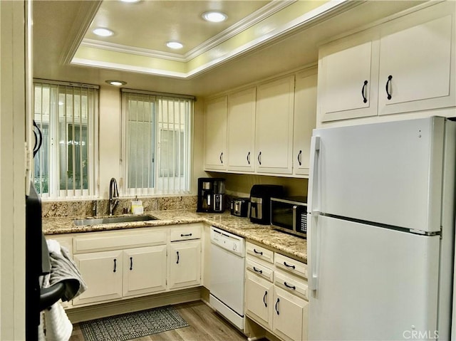 kitchen featuring white appliances, wood finished floors, a tray ceiling, a sink, and crown molding