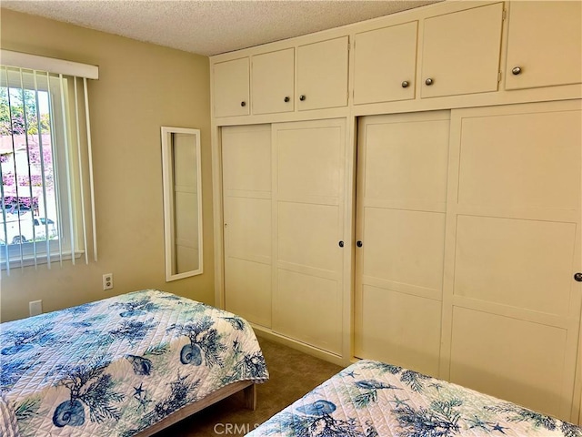 bedroom featuring multiple windows, a closet, dark colored carpet, and a textured ceiling