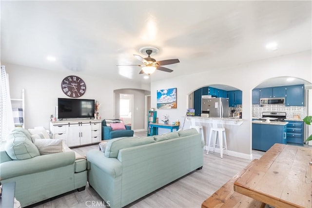 living room featuring ceiling fan, baseboards, arched walkways, and light wood-type flooring