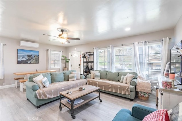 living area with light wood-style flooring, a ceiling fan, baseboards, and a wall mounted air conditioner