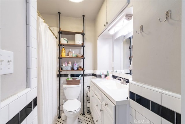 bathroom featuring toilet, a shower with shower curtain, vanity, wainscoting, and tile walls