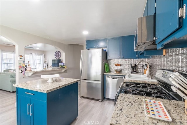 kitchen featuring backsplash, light wood-style flooring, stainless steel appliances, blue cabinets, and a sink