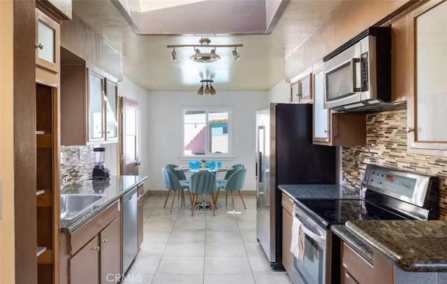 kitchen with baseboards, decorative backsplash, light tile patterned flooring, stainless steel appliances, and a sink