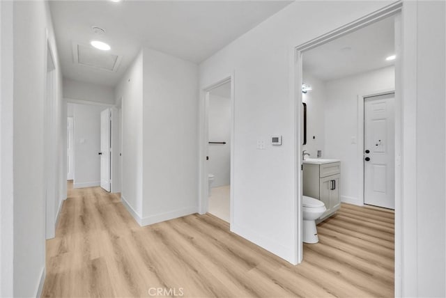 hallway with attic access, light wood-type flooring, and baseboards