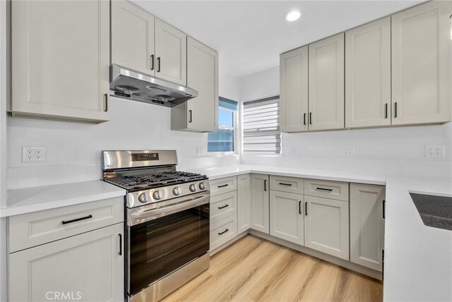 kitchen with light wood-style flooring, under cabinet range hood, recessed lighting, light countertops, and stainless steel gas range