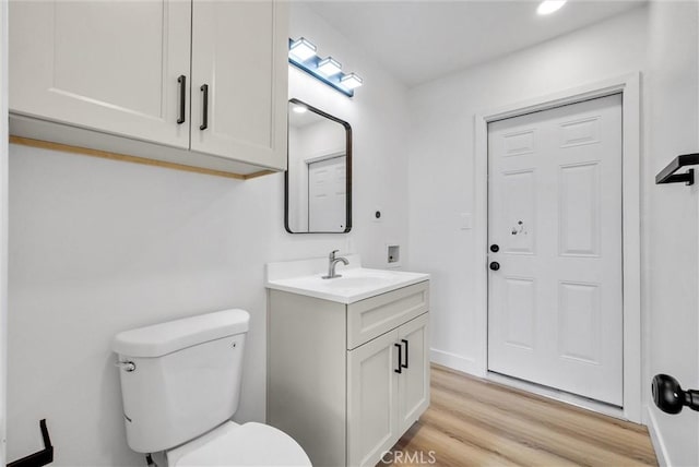 half bath with toilet, wood finished floors, and vanity