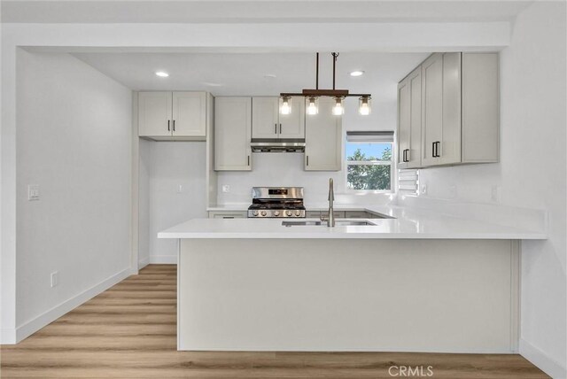 kitchen featuring extractor fan, stainless steel range with gas stovetop, light countertops, a peninsula, and a sink