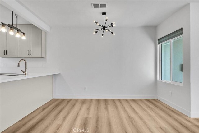 unfurnished dining area with a notable chandelier, light wood-style floors, visible vents, and a sink