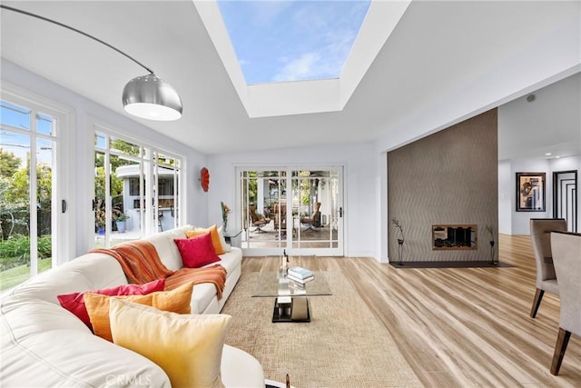 living area featuring lofted ceiling with skylight, plenty of natural light, light wood-style floors, and french doors