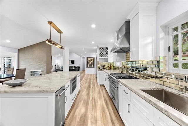 kitchen featuring a kitchen island, light wood-type flooring, stainless steel appliances, wall chimney exhaust hood, and a sink