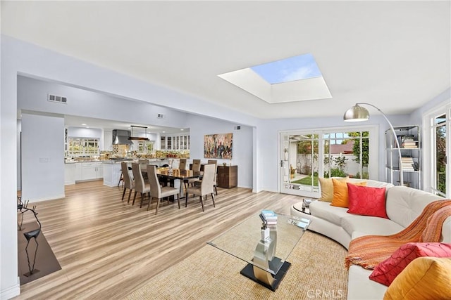 living room with baseboards, visible vents, a skylight, and light wood-style floors