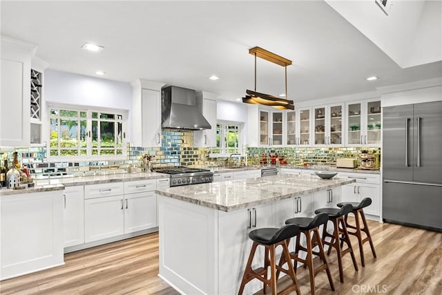 kitchen featuring a sink, stainless steel appliances, wall chimney exhaust hood, white cabinets, and glass insert cabinets