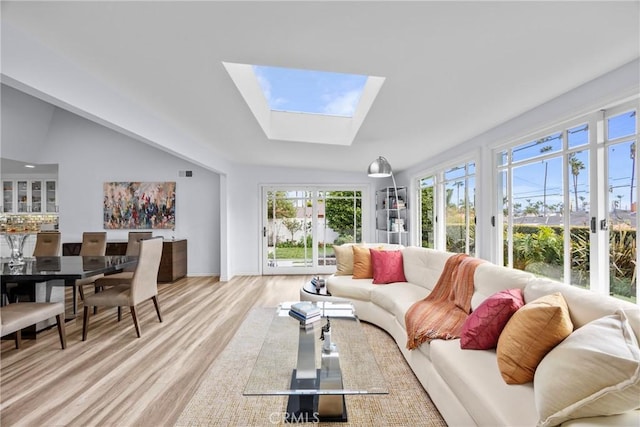 living area featuring light wood finished floors and vaulted ceiling with skylight