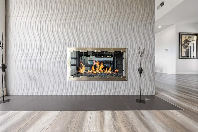 details with visible vents, baseboards, recessed lighting, a warm lit fireplace, and wood finished floors