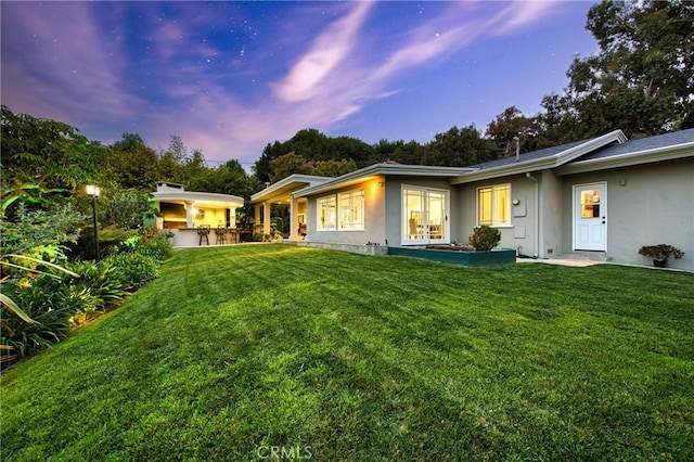 back of house at dusk featuring french doors, a yard, and stucco siding