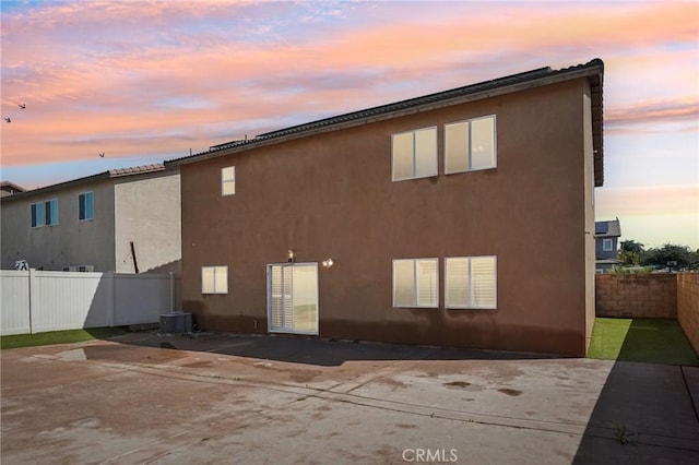 back of property at dusk with stucco siding and fence private yard