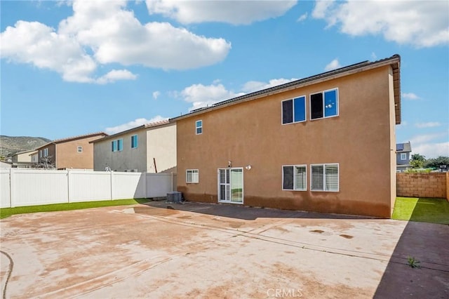 rear view of property with a patio area, central air condition unit, a fenced backyard, and stucco siding