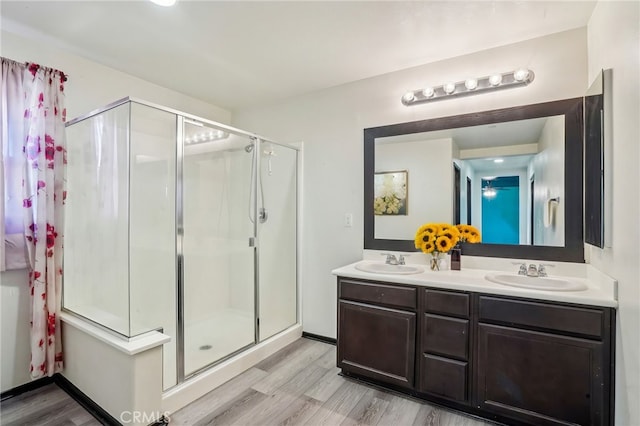 bathroom with double vanity, a shower stall, wood finished floors, and a sink