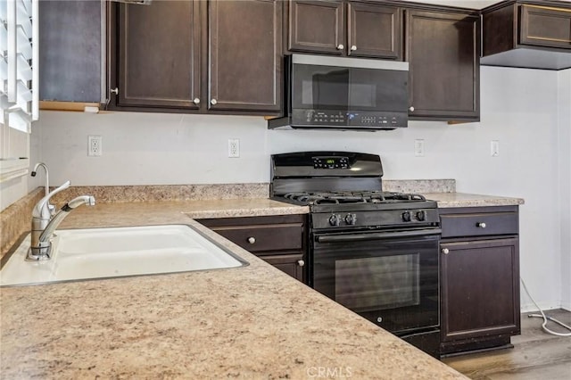 kitchen featuring dark brown cabinetry, black gas range, light countertops, wood finished floors, and a sink