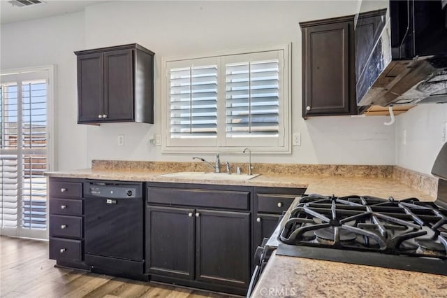 kitchen featuring black appliances, wood finished floors, light countertops, and a sink