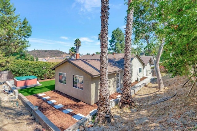 view of side of property with stucco siding, fence, and a shingled roof