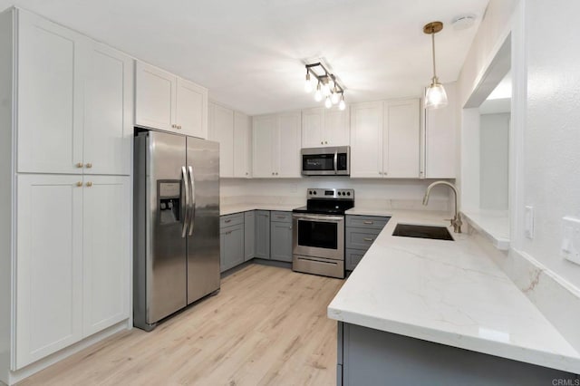 kitchen with gray cabinets, a sink, light stone counters, appliances with stainless steel finishes, and light wood finished floors