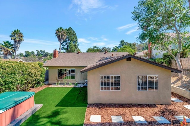 rear view of house with stucco siding, a hot tub, a yard, and fence