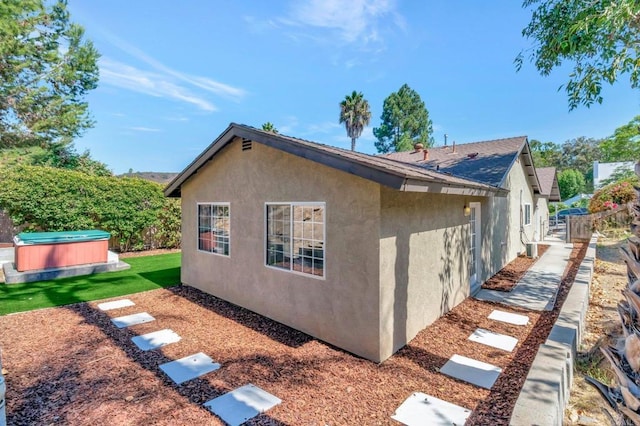 view of side of property with stucco siding, a hot tub, and fence