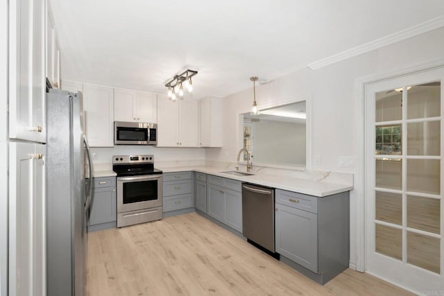 kitchen featuring gray cabinetry, a sink, appliances with stainless steel finishes, crown molding, and light wood finished floors