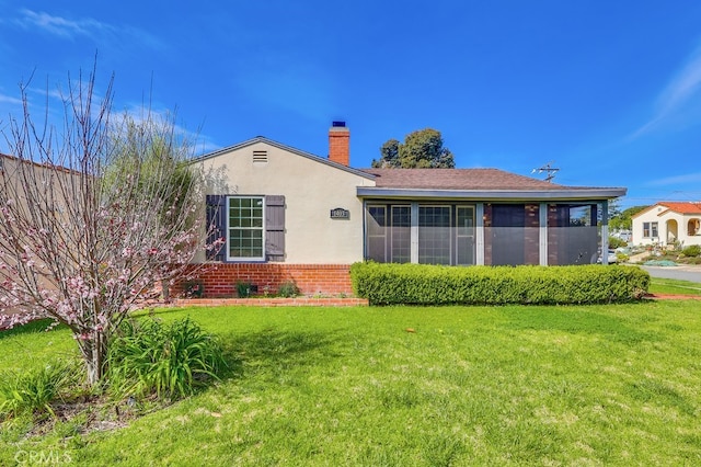 rear view of property with a yard, a sunroom, a chimney, stucco siding, and brick siding