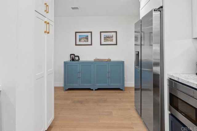 interior space with visible vents, baseboards, light wood-style flooring, blue cabinetry, and appliances with stainless steel finishes