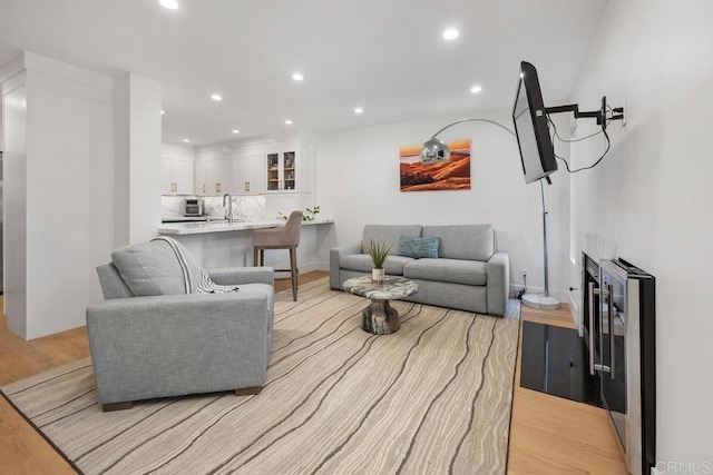 living room with recessed lighting, beverage cooler, a fireplace, and light wood finished floors