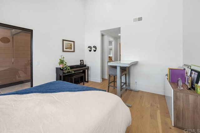 bedroom with visible vents, light wood-style flooring, baseboards, and a towering ceiling