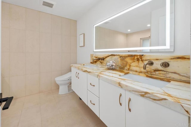 bathroom with tile walls, toilet, visible vents, and a sink