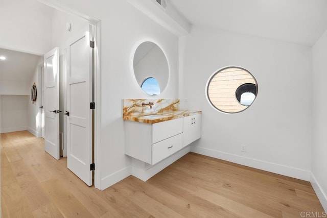 hall featuring light wood-type flooring, baseboards, and vaulted ceiling