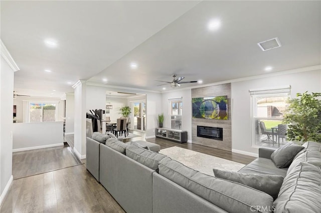 living room featuring visible vents, wood finished floors, a large fireplace, crown molding, and baseboards