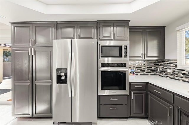 kitchen featuring light countertops, backsplash, appliances with stainless steel finishes, and gray cabinetry