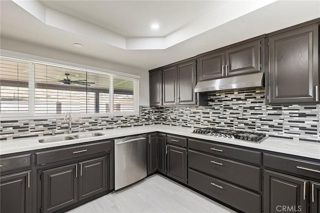 kitchen featuring under cabinet range hood, light countertops, appliances with stainless steel finishes, a raised ceiling, and a sink