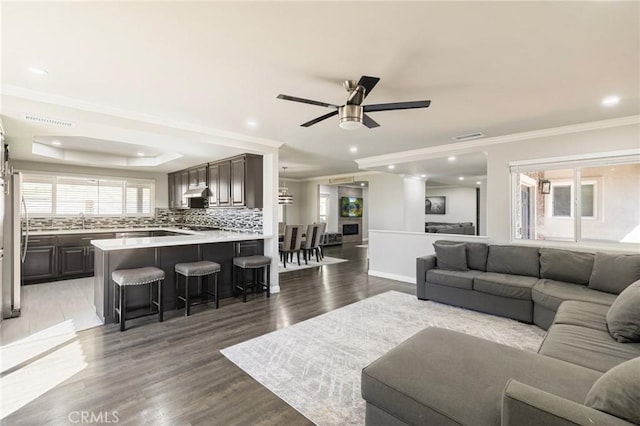 living area featuring visible vents, recessed lighting, light wood-style floors, crown molding, and a raised ceiling