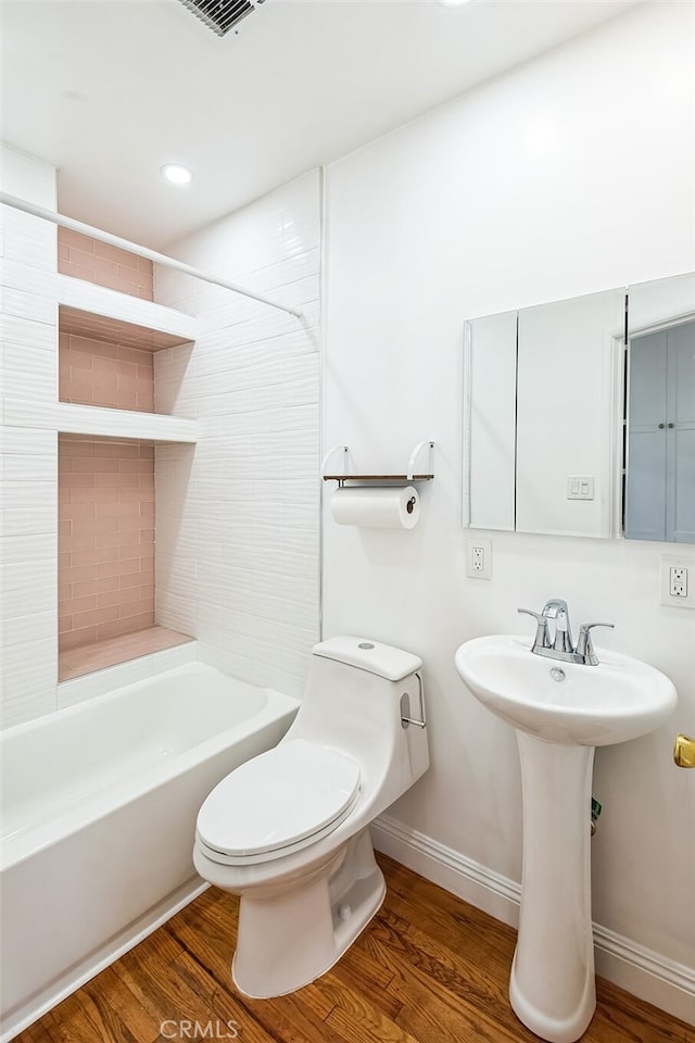 bathroom with toilet, a sink, wood finished floors, washtub / shower combination, and baseboards