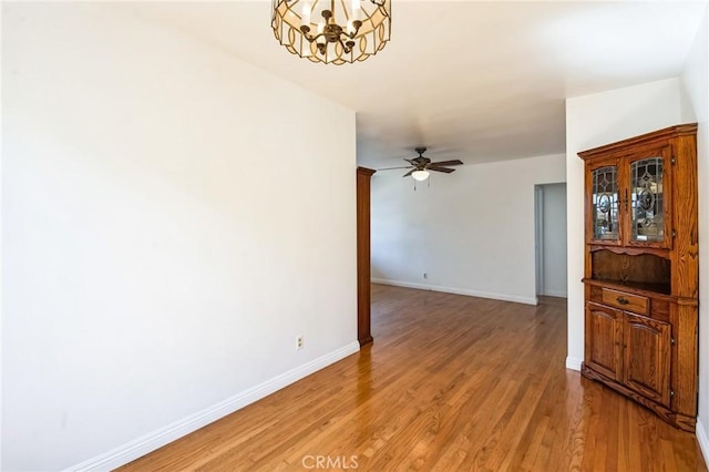 unfurnished room featuring ceiling fan with notable chandelier, baseboards, and light wood finished floors